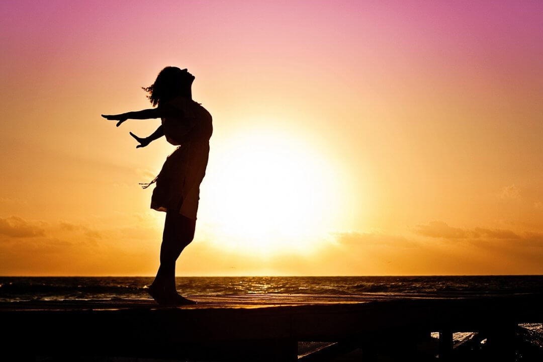Mehr Selbstbewusstsein im Alltag: Strategien für eine stärkere Persönlichkeit, Frau im Sonnenuntergang, die sich streckt